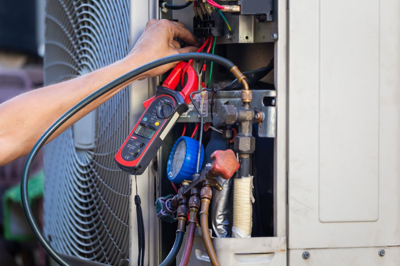 Technician using digital clamp meter to test HVAC system wiring and components