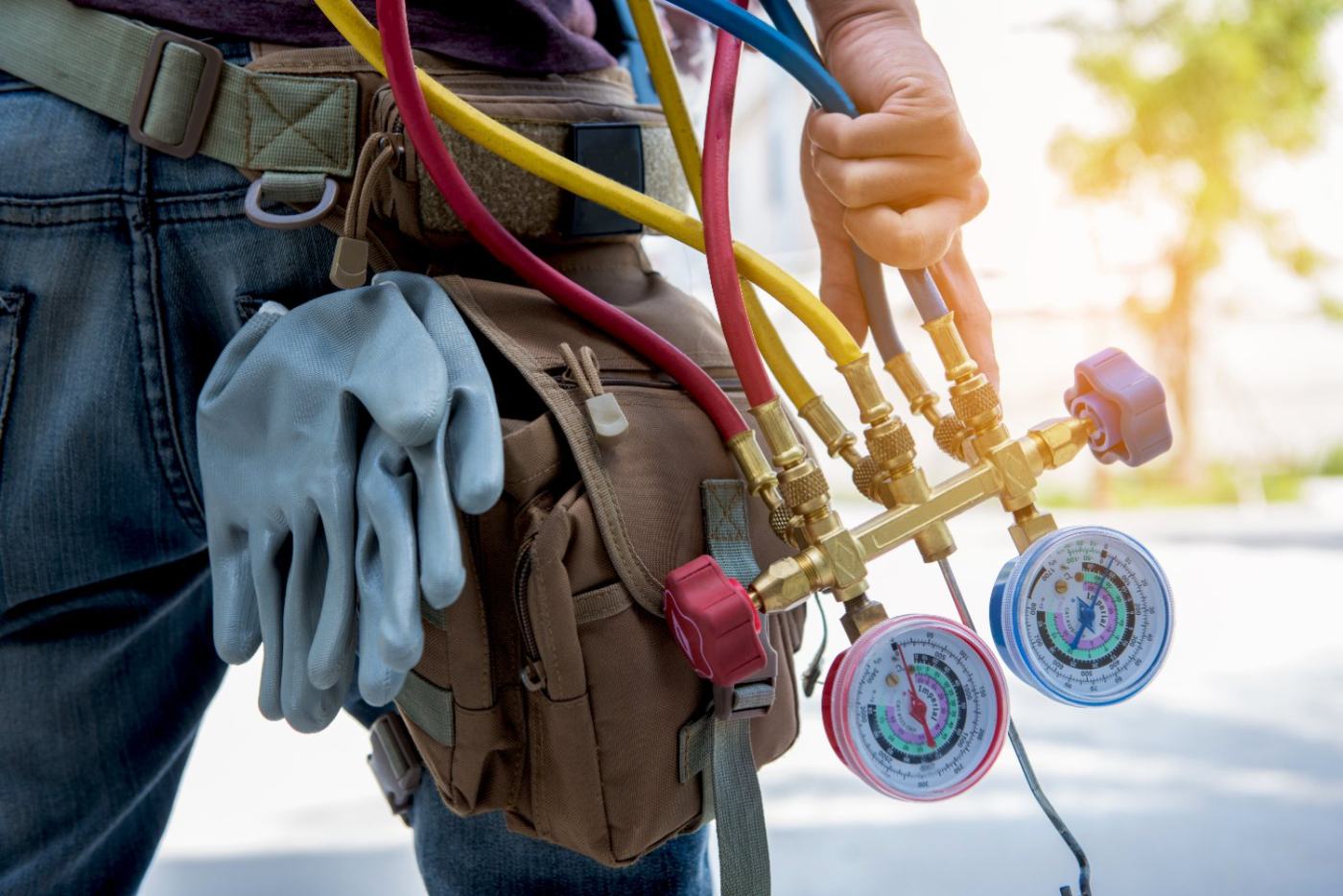 HVAC technician holding refrigerant gauges with colored hoses and tool belt