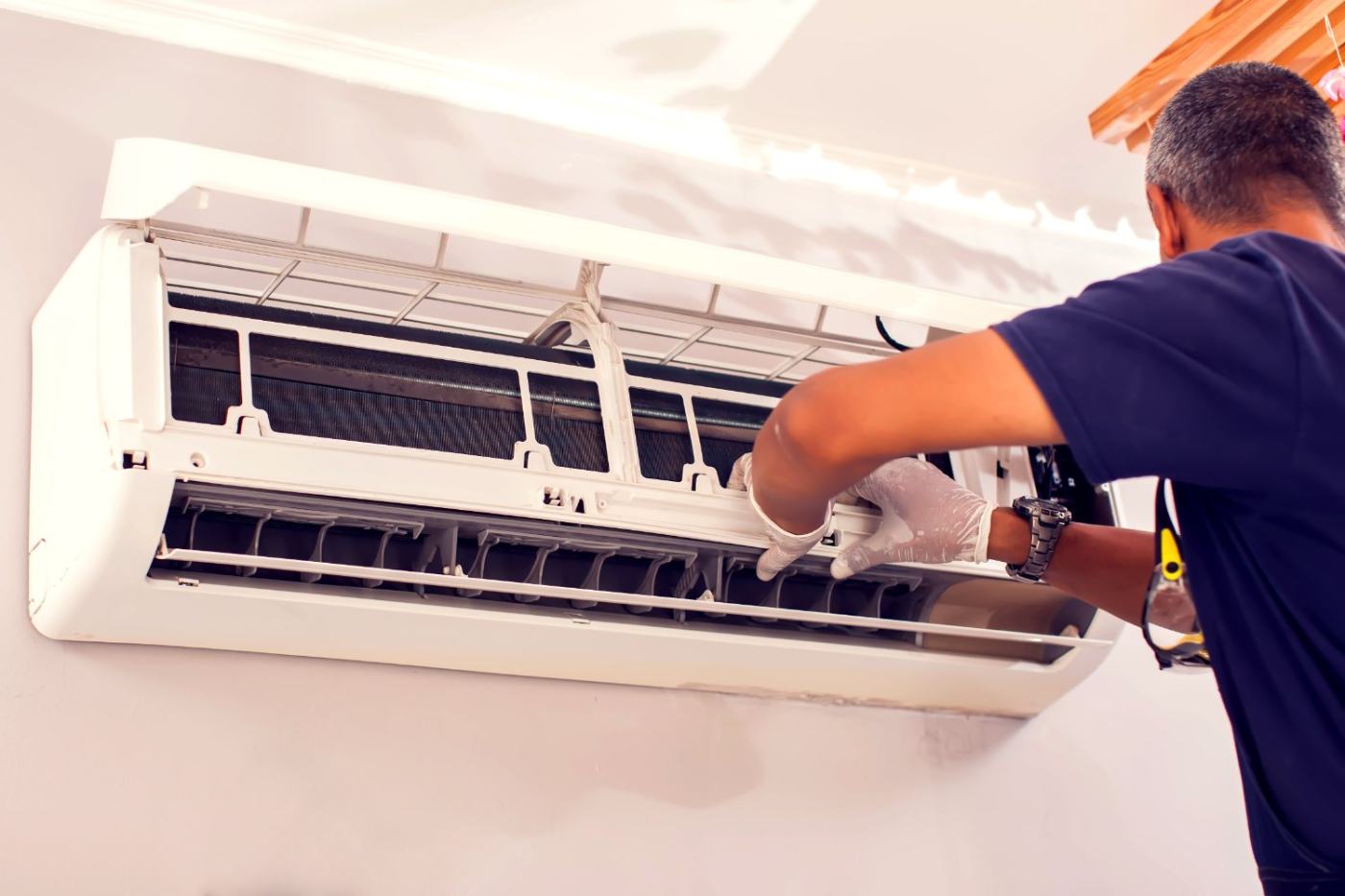 Technician in gloves servicing an open wall-mounted air conditioning unit indoors