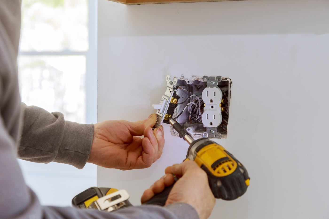 Electrician installing white duplex outlet into wall box with screwdriver