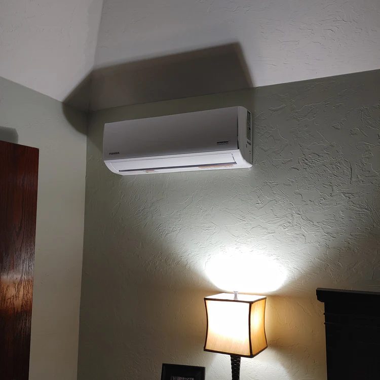 Wall-mounted white air conditioning unit installed on textured beige wall above lamp